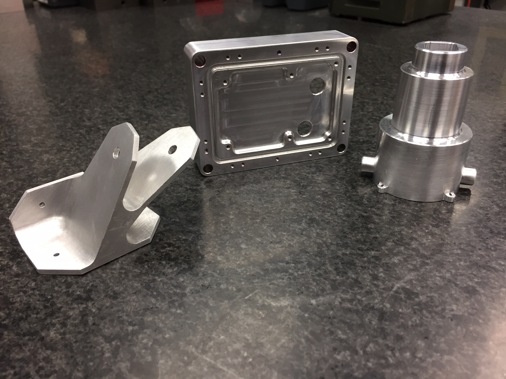 Three precision-machined aluminum components on an inspection table